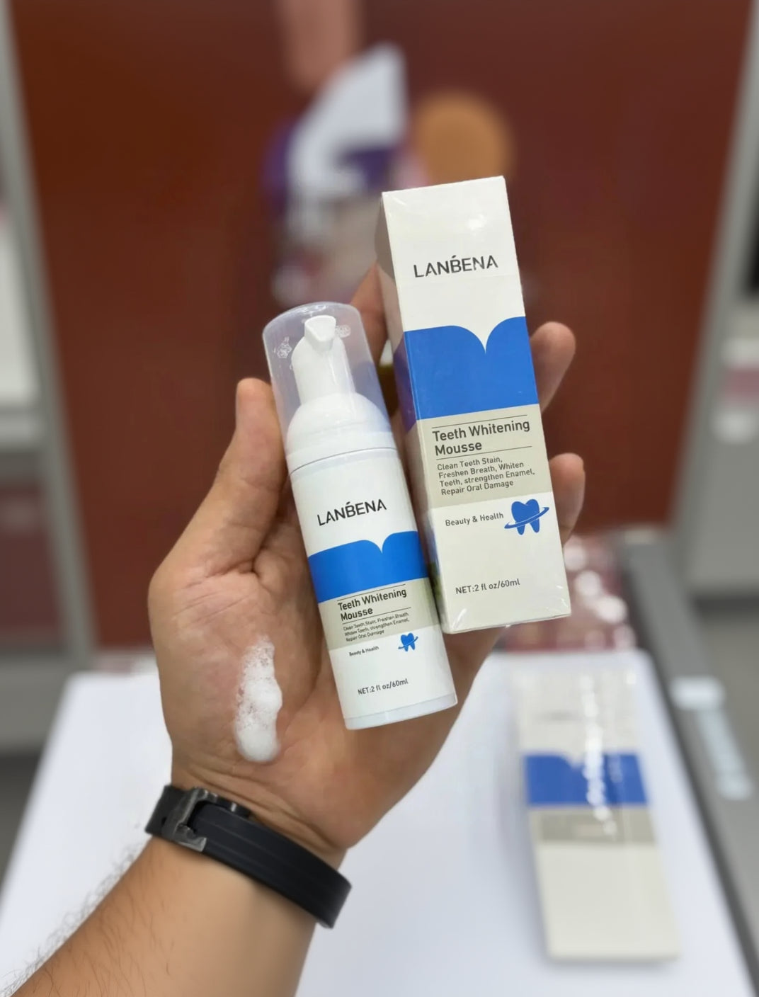 Hand holding Lanbena teeth whitening mousse and packaging against a blurred background